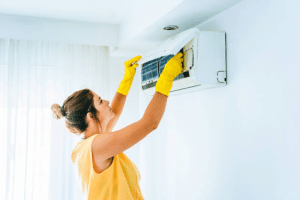 Mujer limpiando la unidad interior de un aire acondicionado split con guantes de protección